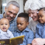 Family reading: Grandparents reading a book to 3 small children who are sitting on their laps. 