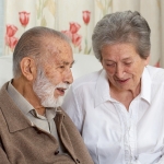 Older couple sitting on the couch smiling at each other. 