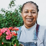 Older woman, with dementia, in the garden holding a pot of red flowers.